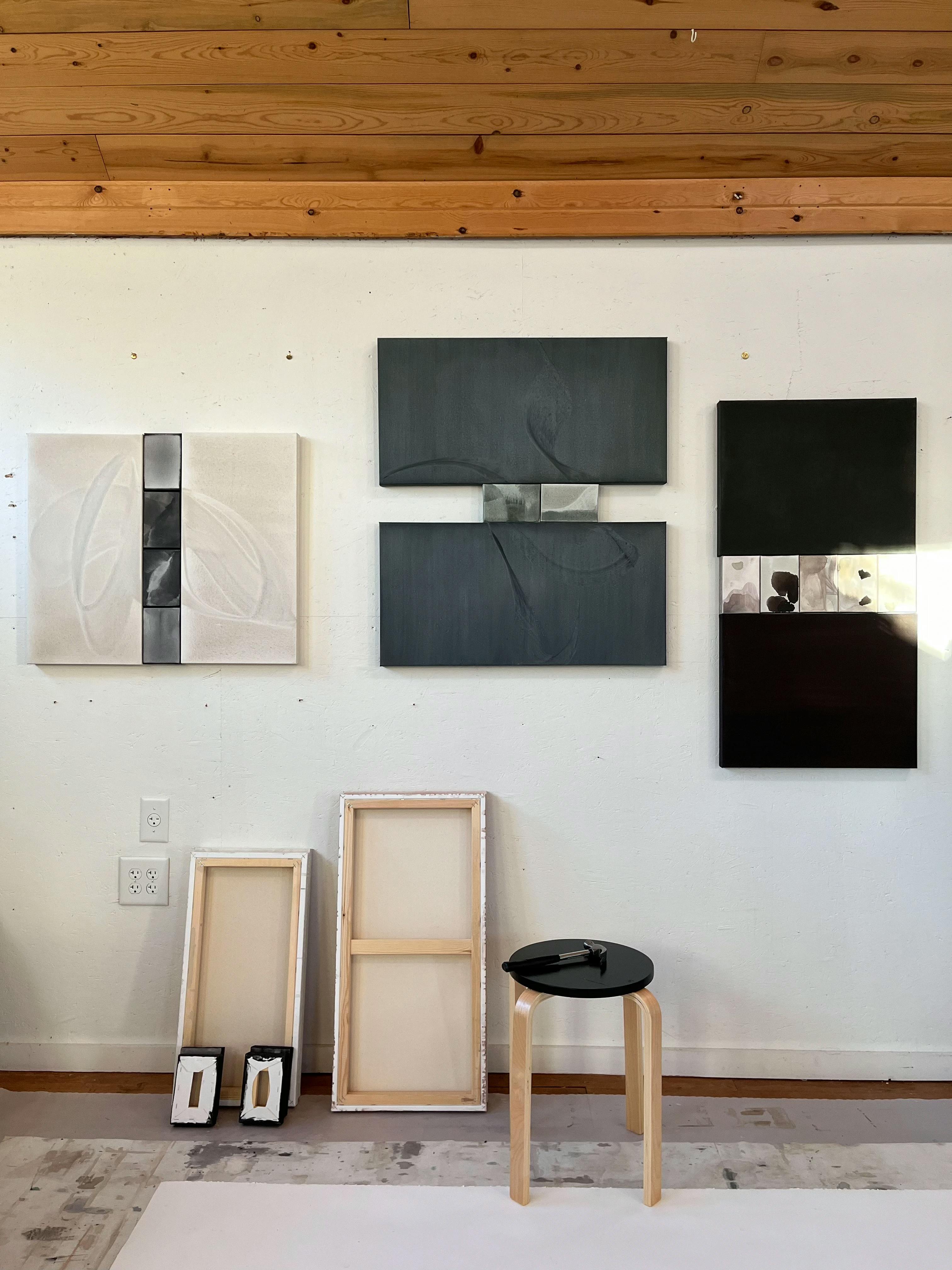 Black and gray diptychs by artist Laura Naples installed on a white wall in her studio above a black wooden stool.