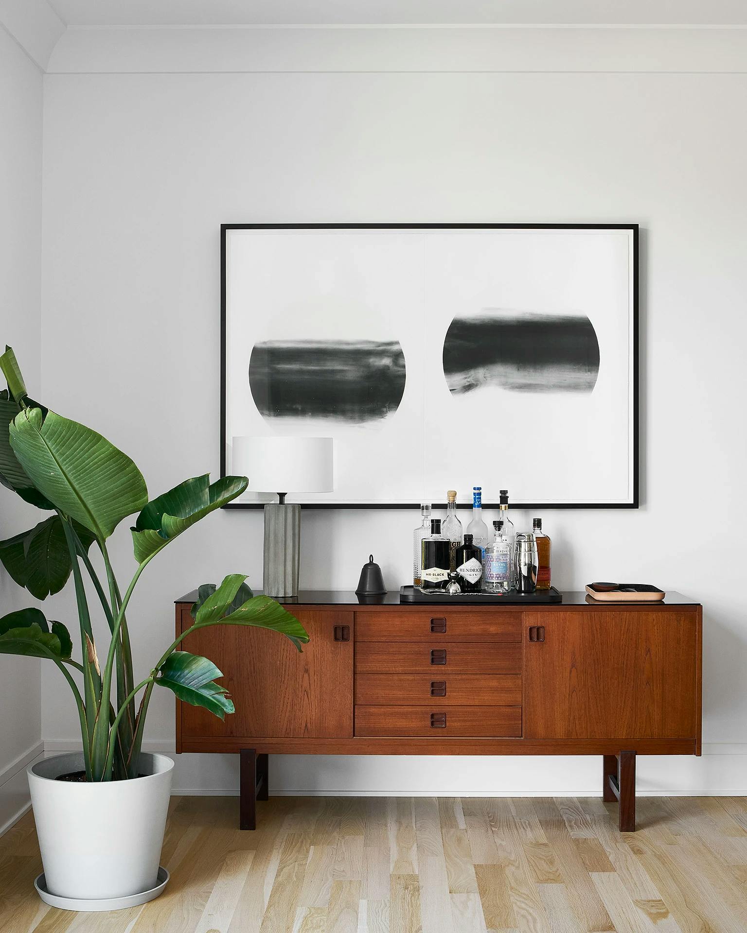 A framed screenprint of two black and white circles by artist Keiko Kamata installed over a wooden console in a Chicago apartment.