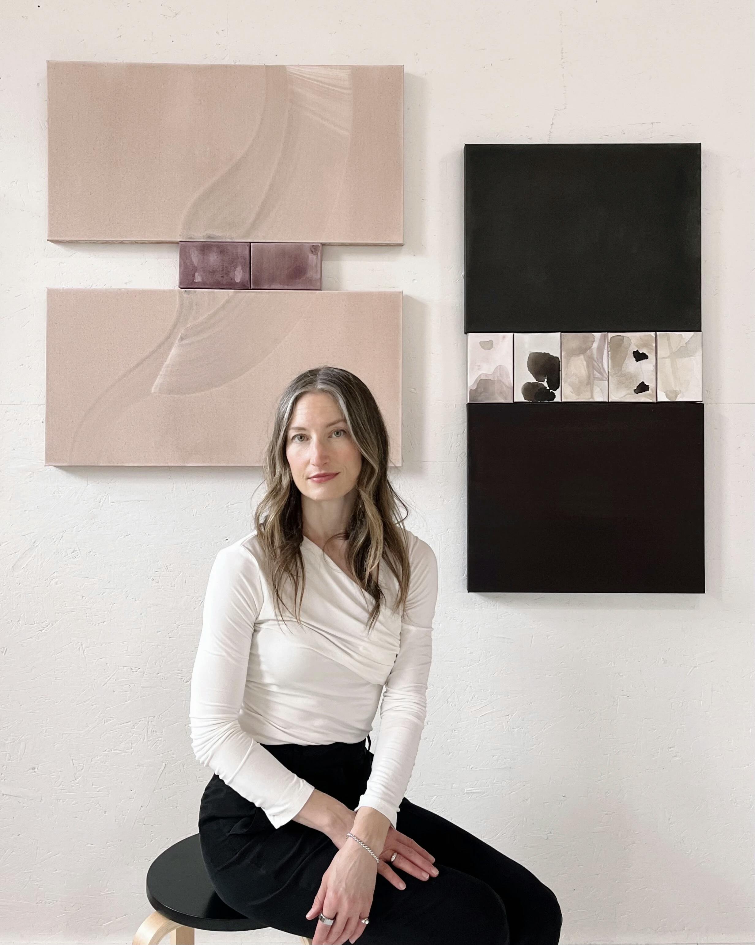 Artist Laura Naples sitting on a stool below her two acrylic wash diptych paintings.